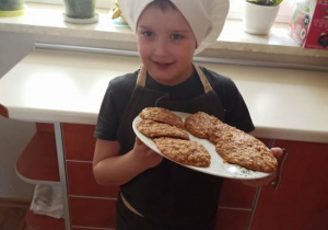 Chłopiec prezentuje na talerzu gotowa do spożycia ciasteczka.